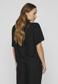 Black short-sleeved top with a relaxed fit and subtle pleated detailing, made from lightweight material. Back view displayed.