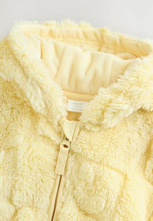 Jachetă pentru bebeluși din fleece galben, cu exterior texturat și pufos, căptușeală moale și închidere cu fermoar. Dispune de o glugă cu margine adunată.