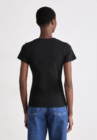 Sort bomulds T-shirt med korte ærmer, rund hals og en tætsiddende silhuet. Bagfra ses en glat tekstur og minimal detaljer.