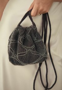 Sac din catifea neagră cu șnur, decorat cu mărgele argintii, având un vârf strâns și două curele răsucite din material.