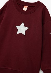 Burgundowa bluza z bawełny z okrągłym dekoltem, z dużą srebrną aplikacją w kształcie gwiazdy z przodu oraz ribbowymi mankietami.