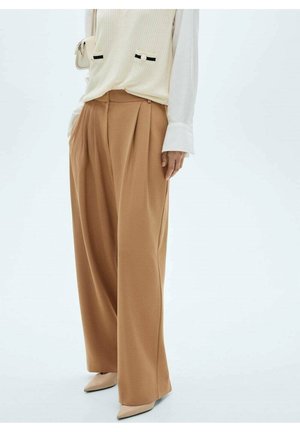 Pantalones beige de pierna ancha con pliegues y textura suave. Combinados con una blusa blanca texturizada que presenta bolsillos y detalles en negro.