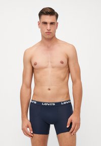 Sötétkék boxer alsónadrág fehér Levi's logóval a derekán. Puha anyag, testhezálló kialakítás, combközép hosszúság.