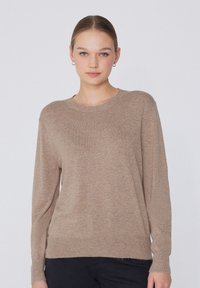 Beige Strickpullover mit langen Ärmeln und Rundhals, verfügt über eine weiche Textur und eine lockere Passform, kombiniert mit schwarzen Hosen.