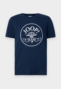 T-shirt en coton bleu marine avec un grand logo circulaire blanc portant le texte "JOOP!" et "JEANS", entouré d'un motif floral et d'une bannière.
