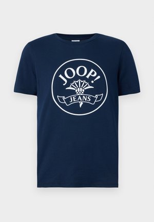 Navy blue cotton T-shirt featuring a large white circular logo with "JOOP!" and "JEANS" text, surrounded by a floral design and banner.
