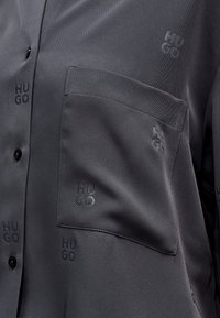 Γκρι πουκάμισο από απαλό ύφασμα με τσέπη-μπαλώμα. Διαθέτει ανάγλυφο μοτίβο με το λογότυπο "HUGO" και κλείσιμο με κουμπιά.