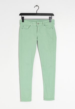 Jeans ajustados de color verde claro, hechos de algodón, con cierre de botón en la parte delantera, cinco bolsillos y una textura lisa. Cuelga de un gancho negro.