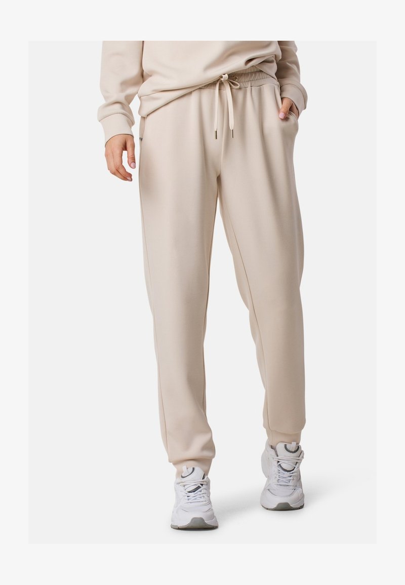 Helle beigefarbene Sweatpants aus weichem Stoff mit elastischem Bund und Kordelzug, ausgestattet mit Seitentaschen und schmal zulaufenden Beinen.