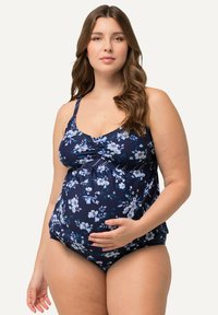 Maillot de bain de maternité en marine avec un motif floral blanc et bleu. Doté de bretelles réglables et d'un corsage ajusté, mettant en valeur un ventre rond.