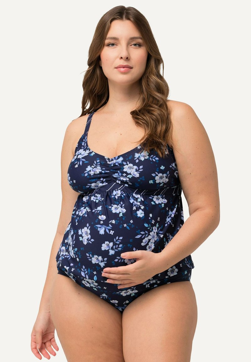 Maillot de bain de maternité en marine avec un motif floral blanc et bleu. Doté de bretelles réglables et d'un corsage ajusté, mettant en valeur un ventre rond.