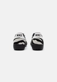 Sneakers Nike in bianco e nero con un motivo a stampa zebra, suola nera uniforme e un tallone bianco con la scritta “NIKE” in nero.