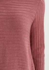Sweter dzianinowy w delikatnym odcieniu różu, charakteryzujący się pionowym prążkowanym wzorem na rękawach oraz poziomymi paseczkami na korpusie. Okrągły dekolt, lekki materiał.