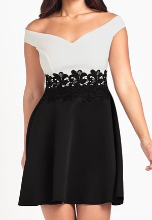 Off-shoulder jurk met een wit aangesloten lijfje, een zwarte rok en zwarte bloemenkant details bij de taille.