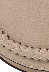 Beige leren handtas met een gestructureerd oppervlak en een decoratief gevlochten accent langs de naad. Zwarte stiksels omlijnen de randen.