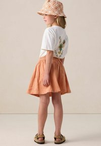 Weißes T-Shirt mit kurzen Ärmeln und Hummer-Grafik, kombiniert mit einem pastellorangefarbenen Rock mit floraler Stickerei und einem gemusterten Bucket Hat.