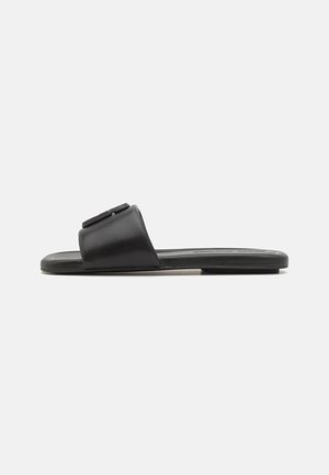 Des sandales noires à glissière en cuir lisse, avec une large lanière au design plat et une semelle intérieure texturée. Style minimaliste, orteils découverts.