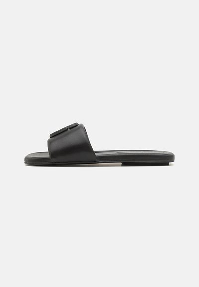 Des sandales noires à glissière en cuir lisse, avec une large lanière au design plat et une semelle intérieure texturée. Style minimaliste, orteils découverts.