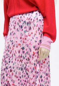 Růžová sukně s multikolorovým abstraktním leopardím potiskem. Lehká látka; nošena s dlouhým rukávem v červené a růžové barvě, který má pruhované manžety.