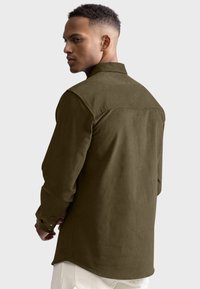 Zielona, długorękawowa koszula z kołnierzykiem i zapinanymi mankietami. Wykonana z teksturowanej tkaniny, ma szew yoke na plecach oraz lekko zaokrąglony dół.