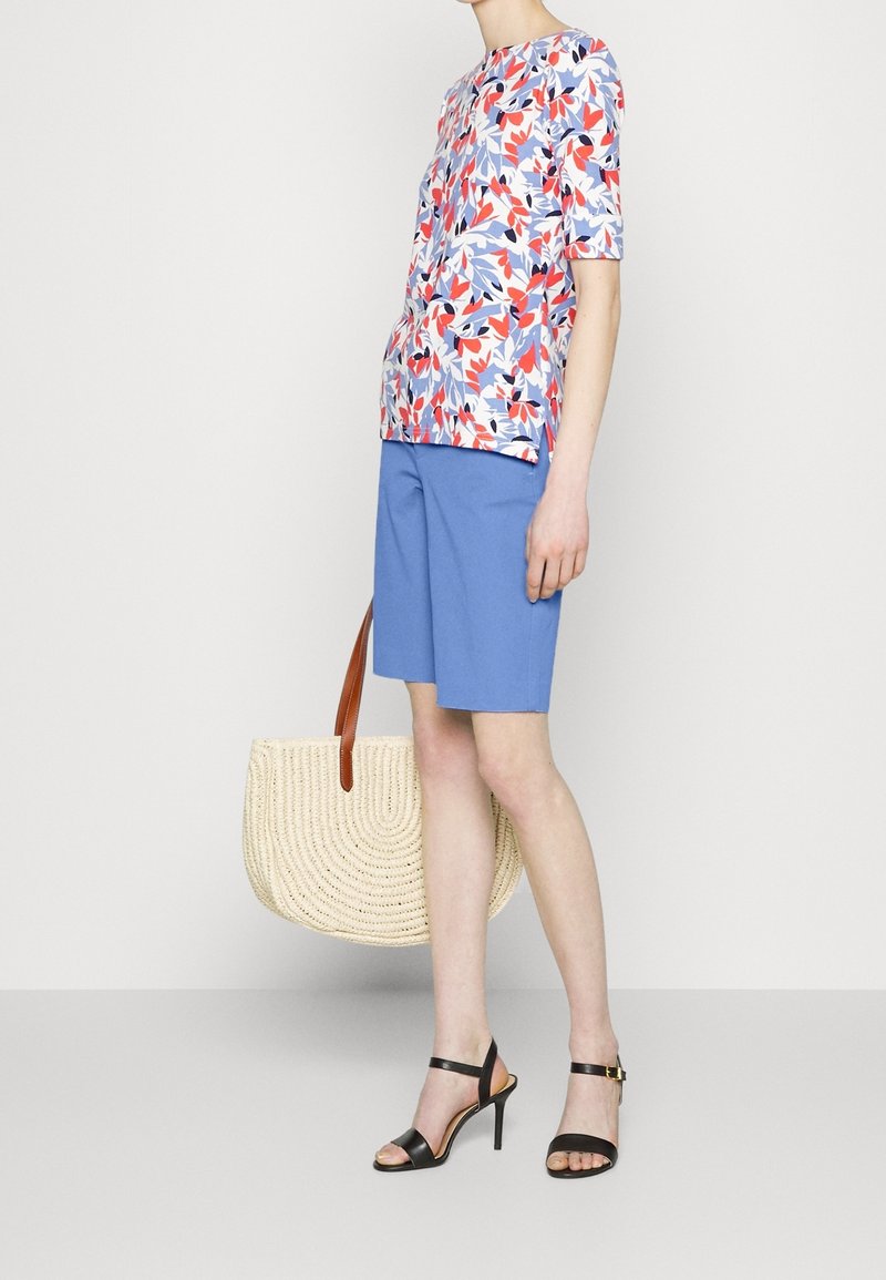 Top a maniche corte con motivo floreale nei toni di rosso, blu e rosa; abbinato a pantaloni corti azzurri chiari e una borsa a tracolla in beige intrecciato. Sandali neri con tacco alto.