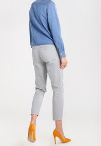 Pantaloni grigi chiari con un design affusolato, abbinati a una camicia di jeans blu e tacchi alti gialli vivaci, che mostrano un look elegante e moderno.