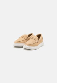 Beige suède instappers met een gestructureerde bovenkant, een witte rubberen zool en gestikte details. Beschikt over twee decoratieve banden over de voorkant.
