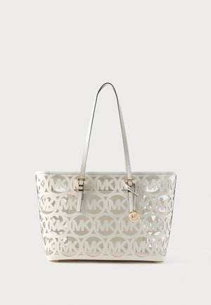 Valge käekott, millel on välja lõigatud ringikujuline "MK" logo muster, kahekordsed õlarihmad ja kuldne ümmargune logo ripats ühe rihma küljes.