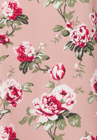 Tecido floral com grandes rosas vermelhas e brancas sobre um suave fundo rosa, complementado por folhas verdes e detalhes finos.