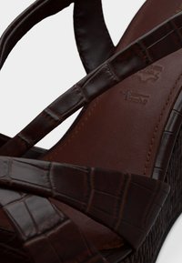 Καφέ πλατφόρμα σανδάλι από συνθετικό δέρμα με υφή εμπνευσμένη από κροκόδειλο. Διαθέτει σταυρωτά λουράκια και λεία, επενδεδυμένη σόλα.