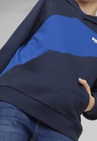 Felpa con cappuccio blu navy con una grande striscia orizzontale blu, tasca a marsupio, bordi e polsini a coste, con un logo sul petto.