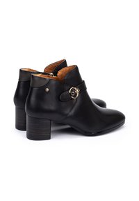 Botas de cuero negro hasta el tobillo con punta afilada, interior marrón y una hebilla dorada decorativa en el lateral. Tacón de madera apilada.
