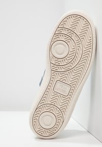 Semelle d'une basket beige Veja avec des motifs circulaires et en chevrons et l'inscription « VEJA wild rubber from Amazonia » embossée au centre.
