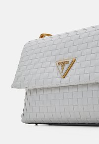 Bolso de mano tejido blanco con un acento dorado en forma de triángulo, que presenta una forma estructurada y una textura suave en la solapa y el cuerpo.