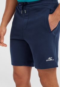 Shorts bleu marine en tissu doux, dotés d'une taille élastique avec cordon de serrage, de poches latérales et d'un logo blanc sur le bas de l'ourlet.