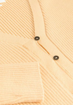 Ribbed, vaalean persikanvärinen neuletakki, jossa on V-kaula-aukko, kaksi mustaa nappia ja pehmeä pinta. Sisältää yhden avoimen taskun hihaassa.