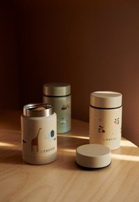 Kolme eristettyä astiaa hillityissä väreissä: yksi eläinkuvioitu, toinen sinisillä korostuksilla, ja yksi yksinkertaiseen kansiin; sileä mattapinta.