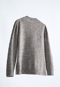 Pull en maille gris avec un col rond, des manches longues et une coupe décontractée. La texture semble douce et légèrement duveteuse.