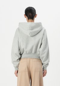 Haut en sweat gris court avec capuche à cordon de serrage, manches amples et ourlet côtelé ; associé à un pantalon beige à jambes larges avec poches au dos.