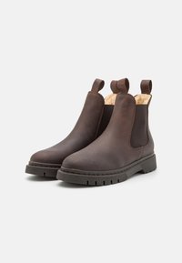 Botas de tobillo de cuero marrón con paneles elásticos laterales y tiradores, que cuentan con una suela de goma texturizada y un forro interior suave.