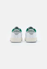 Zapatillas de cuero blanco con acentos en verde y gris, que cuentan con una suela de goma texturizada y un collar acolchado para mayor comodidad. Marca Reebok en el talón.