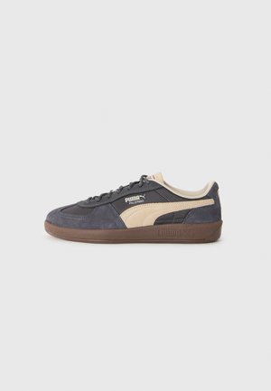 Puma Palermo tennisjalatsid on tumedast mereväe mürgaülemisest, beežidest aktsentidest ja pruuni kummi tallast, millel on tekstuuritud viimistlus.