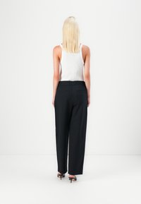 Black wide-leg trousers with a smooth texture, tailored waistband, and pockets, paired with a white sleeveless top.