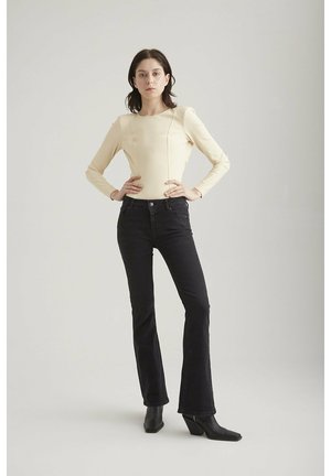 Cream long-sleeve top with a smooth texture, paired with black flared jeans. Tall black heeled boots complete the outfit against a neutral background.