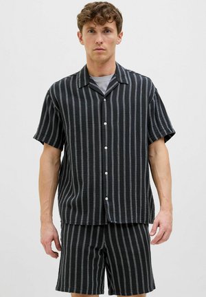 Chemise noire à manches courtes avec boutons et shorts assortis, tous deux avec des rayures verticales blanches, offrant une coupe décontractée et un tissu texturé.