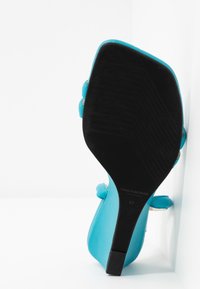 Semelle et talon noirs d'une sandale à talons hauts turquoise avec des lanières, taille 37, positionnée sur un fond blanc.