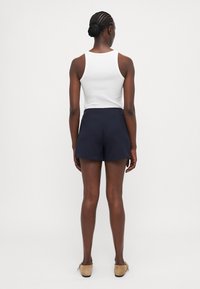 Navy shorts with a smooth texture, slim fit, and a mid-rise waist. Paired with a white tank top and tan shoes.