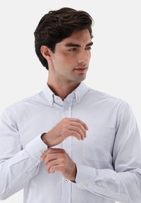 Himmelblau und weiß gestreifte Button-up-Bluse mit Kragen, langen Ärmeln und einer Brusttasche. Verfügt über kleine Knopfakzente an den Manschetten.