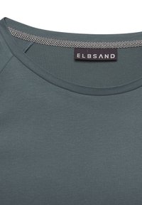 Dunkeltürkisfarbenes Rundhals-T-Shirt mit glatter Textur und einem Herringbone-Muster am Kragen; trägt ein gesticktes Etikett mit der Aufschrift "ELBSAND."