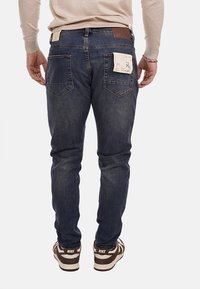 Jeans in denim blu scuro con una vestibilità slim, tasche visibili e un'etichetta in pelle in vita. Abbinati a sneakers marroni e bianche.